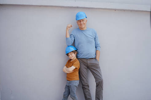 Selbstbewusster älterer Mann und Junge mit Schutzhelm vor einer Mauer - JOSEF12209