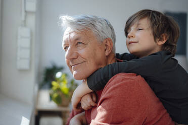 Thoughtful boy embracing grandfather from behind at home - JOSEF12225