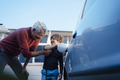 Happy senior man and grandson charging electric car - JOSEF12227