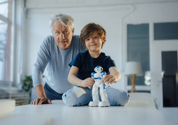 Smiling boy playing with robot model by grandfather at home - JOSEF12233