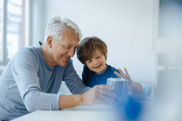 Lächelnder älterer Mann und Enkel bei der Prüfung eines Heizmoduls zu Hause - JOSEF12234