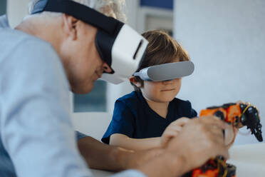 Großvater und Enkel mit VR-Brille beobachten Robotermodell zu Hause - JOSEF12237