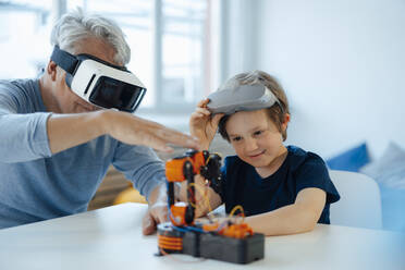 Boy examining robot model by grandfather with VR glasses at home - JOSEF12239