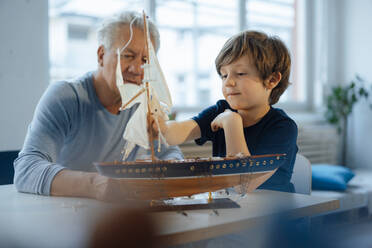Junge und älterer Mann betrachten ein Schiffsmodell auf einem Tisch - JOSEF12240
