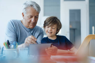 Lächelnder älterer Mann, der von seinem Enkel zu Hause auf einem Tablet-PC gezeichnet wird - JOSEF12243