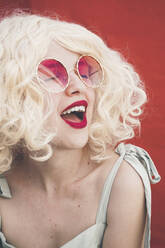 Fröhliche blonde Frau mit Sonnenbrille vor rotem Hintergrund - SVCF00124