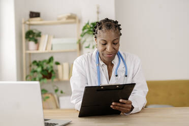 Smiling doctor with clipboard working at home office - JCZF01063