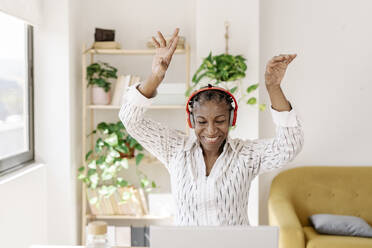 Happy woman wearing wireless headphones dancing at home - JCZF01080