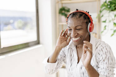 Smiling woman listening music through wireless headphones at home - JCZF01082