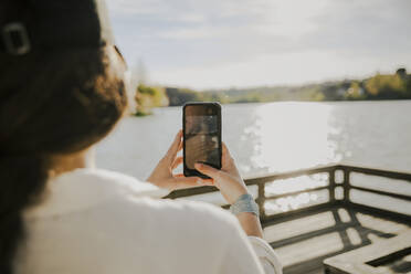 Junge Frau fotografiert mit ihrem Smartphone an einem sonnigen Tag - ACPF01451