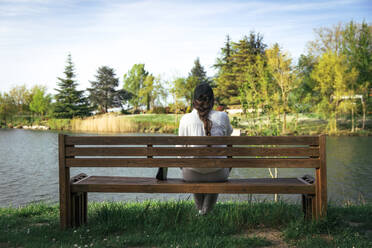 Junge Frau sitzt auf einer Bank vor einem See im Park - ACPF01454