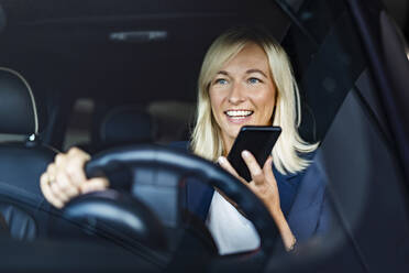 Geschäftsfrau, die über Lautsprecher telefoniert und Auto fährt, gesehen durch die Windschutzscheibe - DIGF18626