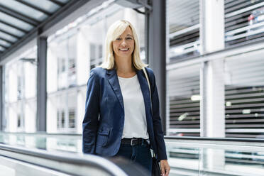 Smiling businesswoman standing on moving walkway - DIGF18629