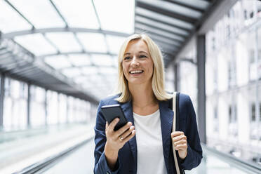 Smiling businesswoman with phone standing on moving walkway - DIGF18632