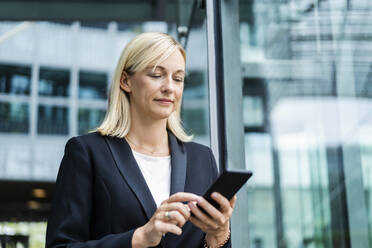 Blonde Geschäftsfrau, die eine SMS über ihr Smartphone schreibt - DIGF18639