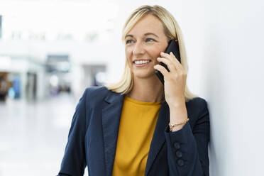 Smiling businesswoman talking over phone leaning on wall - DIGF18661
