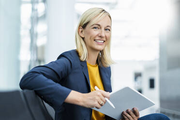 Lächelnde Geschäftsfrau mit blondem Haar hält Tablet-PC - DIGF18669