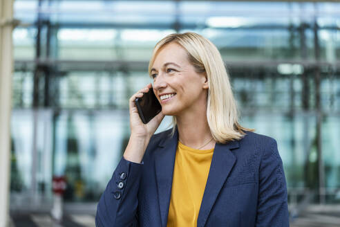 Glückliche Geschäftsfrau im Gespräch am Telefon vor einem Gebäude - DIGF18680