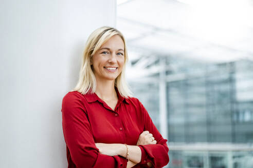 Smiling blond businesswoman standing in front of column - DIGF18698