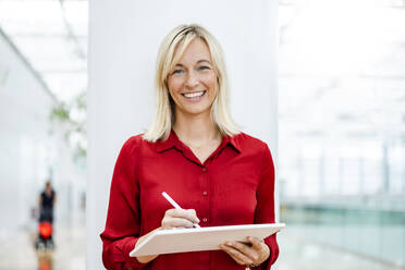 Smiling businesswoman with tablet PC and digitized pen standing in front of column - DIGF18700