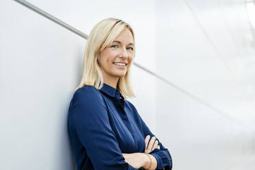 Smiling businesswoman with arms crossed leaning on white wall - DIGF18707