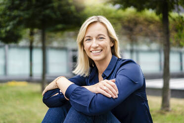 Happy blond businesswoman sitting in park - DIGF18723