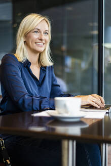 Smiling businesswoman with laptop sitting in coffee shop - DIGF18732