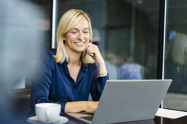 Smiling freelancer using laptop sitting in coffee shop - DIGF18734