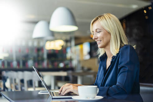 Smiling freelancer typing on laptop sitting at cafe - DIGF18735