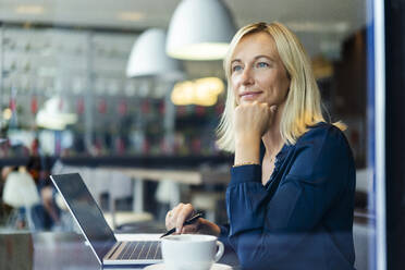 Nachdenkliche Geschäftsfrau mit Laptop in einem Café sitzend - DIGF18736