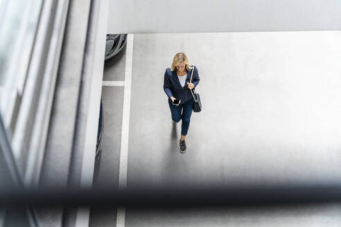 Mature businesswoman using phone walking at parking lot - DIGF18742