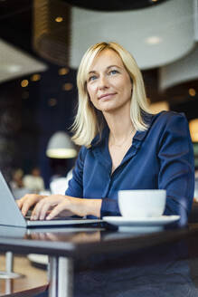 Lächelnde Geschäftsfrau mit Laptop am Tisch in einem Café - DIGF18744