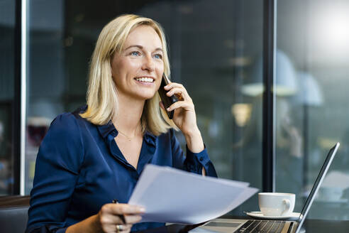 Lächelnde Geschäftsfrau, die am Tisch in einem Café mit ihrem Smartphone telefoniert - DIGF18751