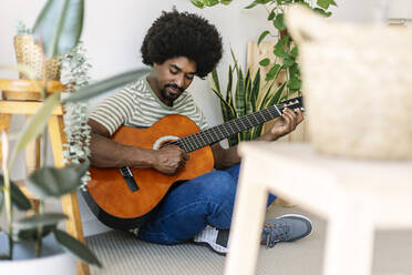 Mann übt Gitarre inmitten von Pflanzen zu Hause - XLGF03028
