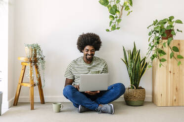 Glücklicher Mann, der einen Laptop benutzt und zu Hause vor einer Wand sitzt - XLGF03032