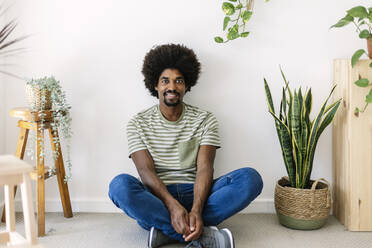 Lächelnder Mann mit Afrofrisur sitzt vor einer Wand - XLGF03038