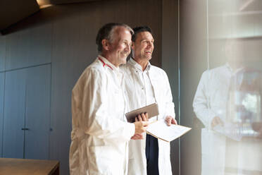 Glückliche Ärzte schauen aus einer Glaswand im Krankenhaus - JOSEF12253