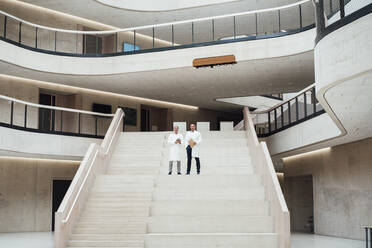 Doctors standing on staircase in hospital lobby - JOSEF12255