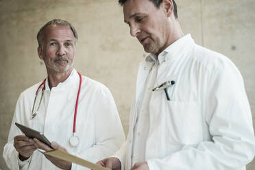 Oberarzt mit Tablet-PC neben einem Kollegen, der sich eine Akte im Krankenhaus ansieht - JOSEF12280