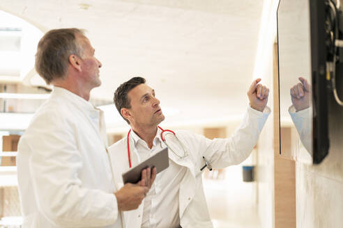 Arzt erklärt Kollegin durch Bildschirm an der Wand im Krankenhaus - JOSEF12283