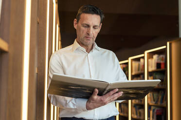 Man reading magazine in illuminated library - JOSEF12341