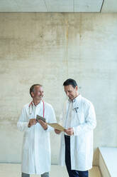 Lächelnde Ärzte mit Akte und Tablet-PC vor einer Wand im Krankenhaus stehend - JOSEF12366