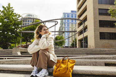 Smiling young woman sitting on staircase at Hafencity - IHF01149