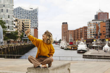 Happy woman taking selfie through smart phone at Elbphilharmonie in Hafencity - IHF01159