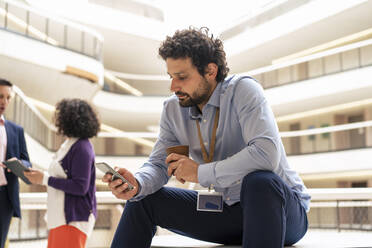 Geschäftsmann Textnachrichten auf Smartphone mit Kollegen diskutieren im Hintergrund im Büro - JOSEF12388