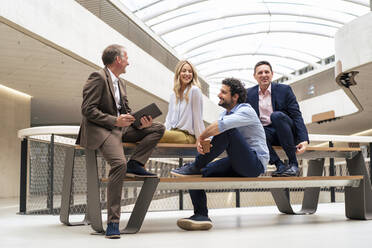 Glückliche Geschäftskollegen, die am Tisch sitzend im Büro eine Strategie diskutieren - JOSEF12394