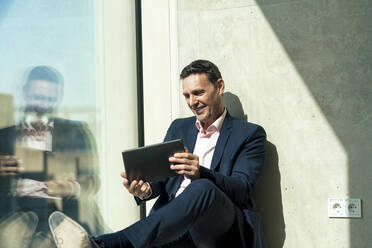 Lächelnder Geschäftsmann mit Videogespräch über Tablet-PC am Fenster im Büro - JOSEF12416