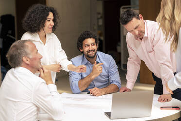 Smiling businessman discussing over document with colleagues in corridor - JOSEF12518