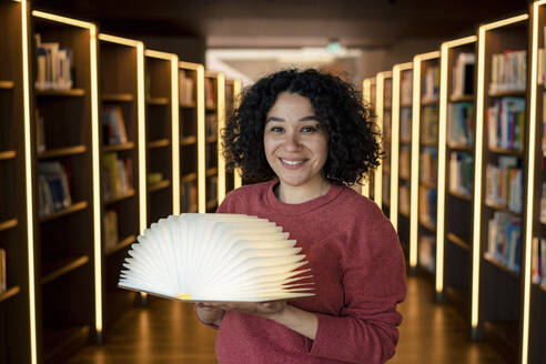 Lächelnder Lehrer mit offener Bücherlampe in beleuchteter Bibliothek - JOSEF12571