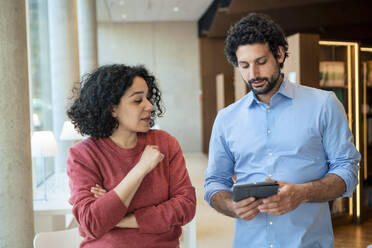 Professor diskutiert über Tablet-PC mit Kollege in Bibliothek - JOSEF12577